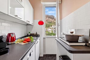 A narrow kitchen with white cabinets, a black countertop, a red kettle, and a window with a view of houses. - La Caravella: Stresa Lake & Islands View Balcony, Stresa, Italy (Stresa)