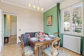 A dining area with a wooden table set for four, a sofa, and a view of a mountain through a window. - La Caravella: Stresa Lake & Islands View Balcony, Stresa, Italy (Stresa)