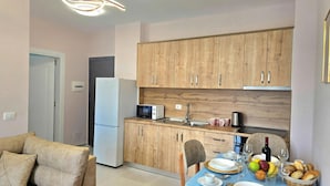 Una cocina funcional con armarios de madera, microondas y un lavamanos. Hay una mesa de comedor con platos, vasos y un bol de fruta.