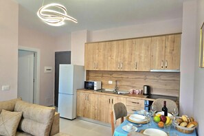 Una cocina funcional con armarios de madera, microondas y un lavamanos. Hay una mesa de comedor con platos, vasos y un bol de fruta.