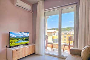 Ein modernes Wohnzimmer mit Fernseher, Holzschränken, einer Couch und einer großen Schiebeglastür, die auf einen Außenbalkon führt.
