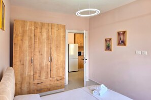 Une chambre à coucher avec un lit, une armoire en bois, un luminaire blanc au plafond et une vue sur la cuisine.