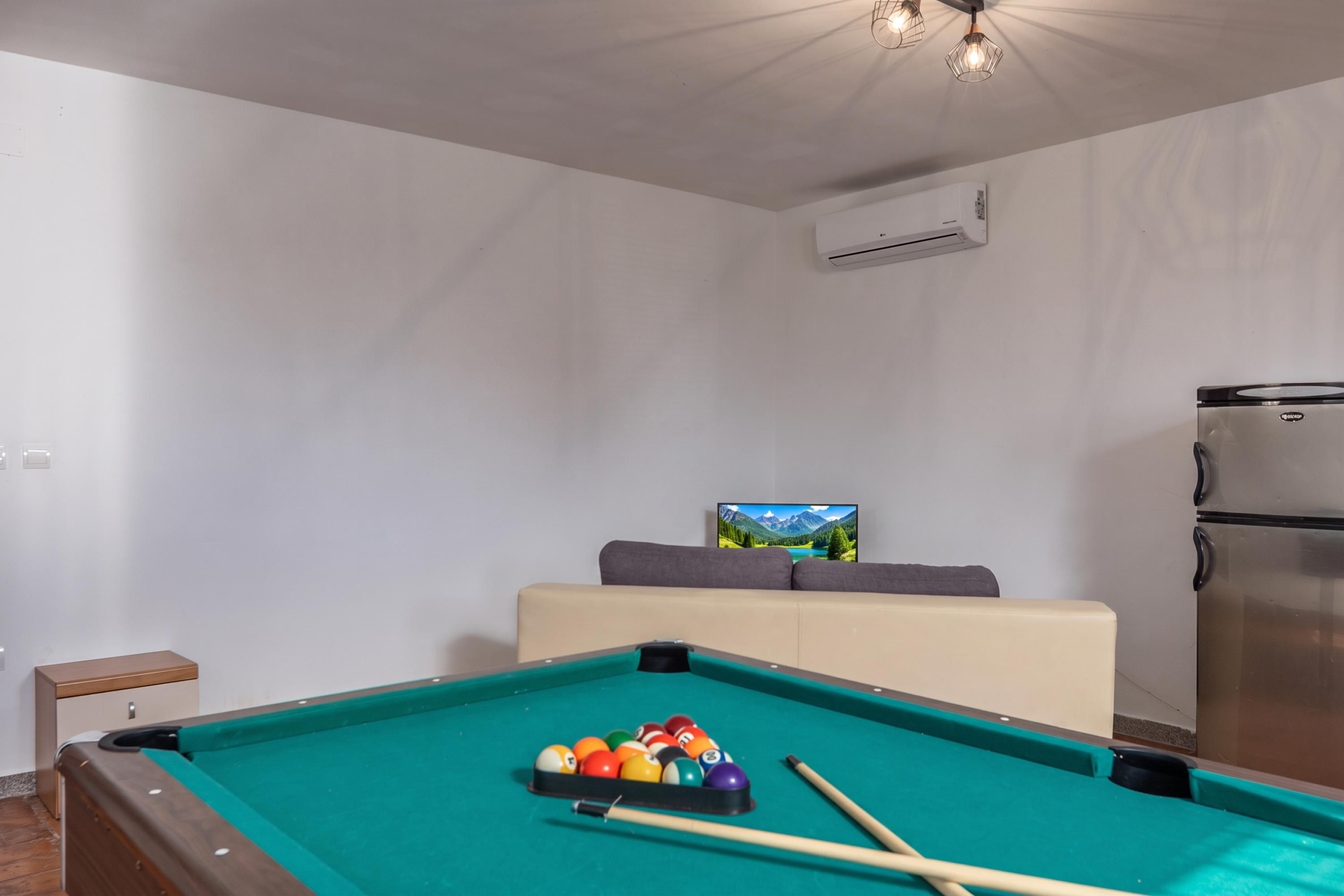 Une table de billard avec des billes, un canapé, un réfrigérateur et un tableau accroché au mur.