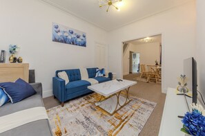 A modern living room with a blue sofa, a white coffee table, and a painting on the wall. - Beautiful 3 bedroom apartment sleeps 7/Near station (Crewe)