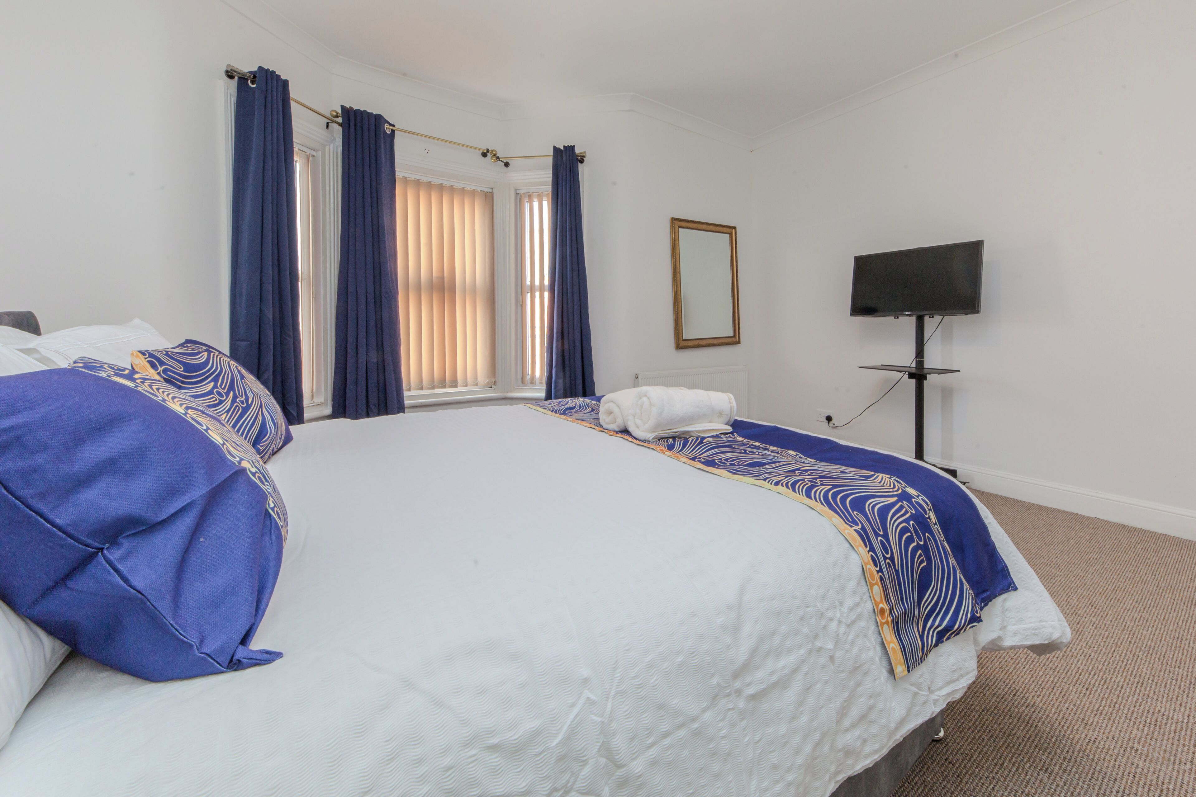 A hotel room with a large bed, a flat-screen TV, and a window with curtains.