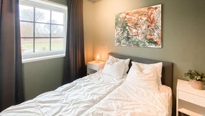 Ein ordentlich bezogenes Bett mit weißen Laken, eine Nachttischlampe und ein Gemälde an der Wand.