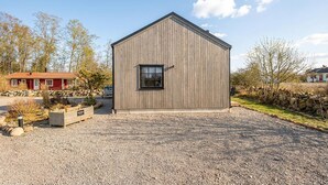 Ein eingeschossiges Holzhaus mit geneigtem Dach, einem kleinen Fenster und einer Schotterauffahrt.