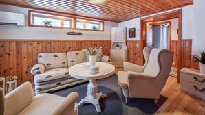 Ett mysigt rum med träpanel på väggarna, en soffa, fåtöljer, ett litet bord med en vas och ett skåp.