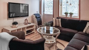 Ett vardagsrum med en stor tv-apparat med platt skärm, ett soffbord i glas och en soffa. Det finns ett TV-bord i trä med en växt och en lykta på.