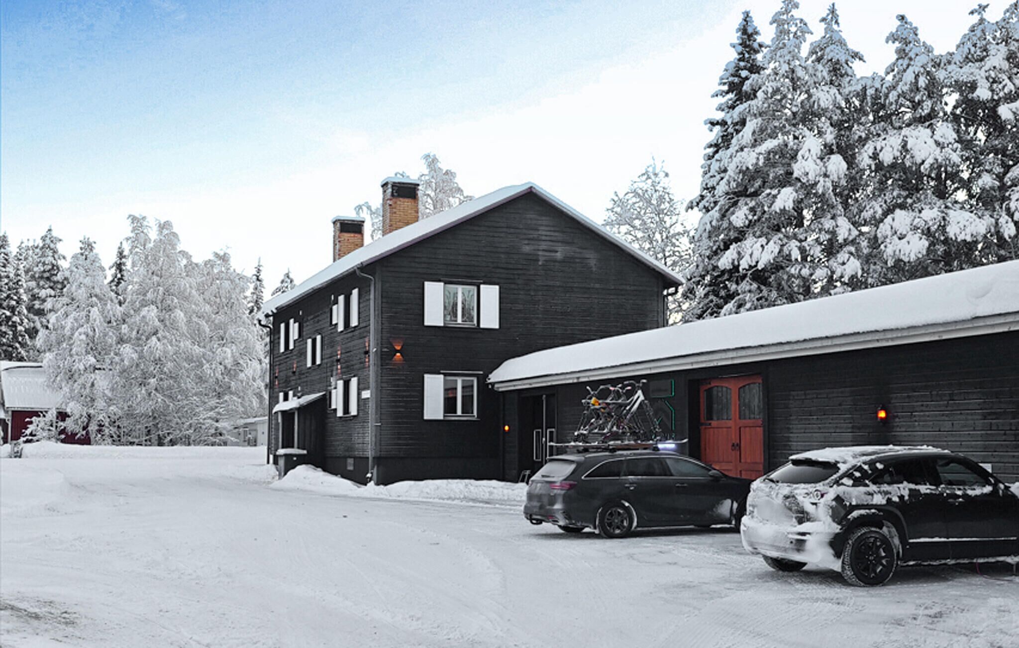 Ein zweistöckiges Haus mit dunkler Fassade, einer roten Tür und einer Garage, vor der Fahrräder stehen.