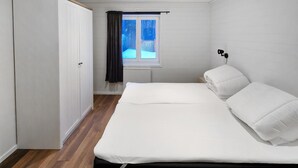 A bedroom with a bed, a window with curtains, a wardrobe, and a bedside table with a lamp.