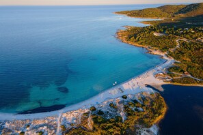 An aerial view of a coastal area with a beach, clear blue waters, and surrounding greenery. - Apposentu, Lu Fraili, Italy (Lu Fraili)