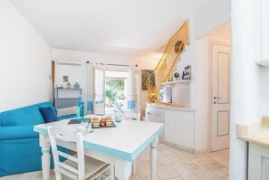 Ein heller, gut beleuchteter Raum mit einem weißen Tisch und einem blauen Sofa, einer Treppe mit gelander und einer Tür mit blauem Rahmen.