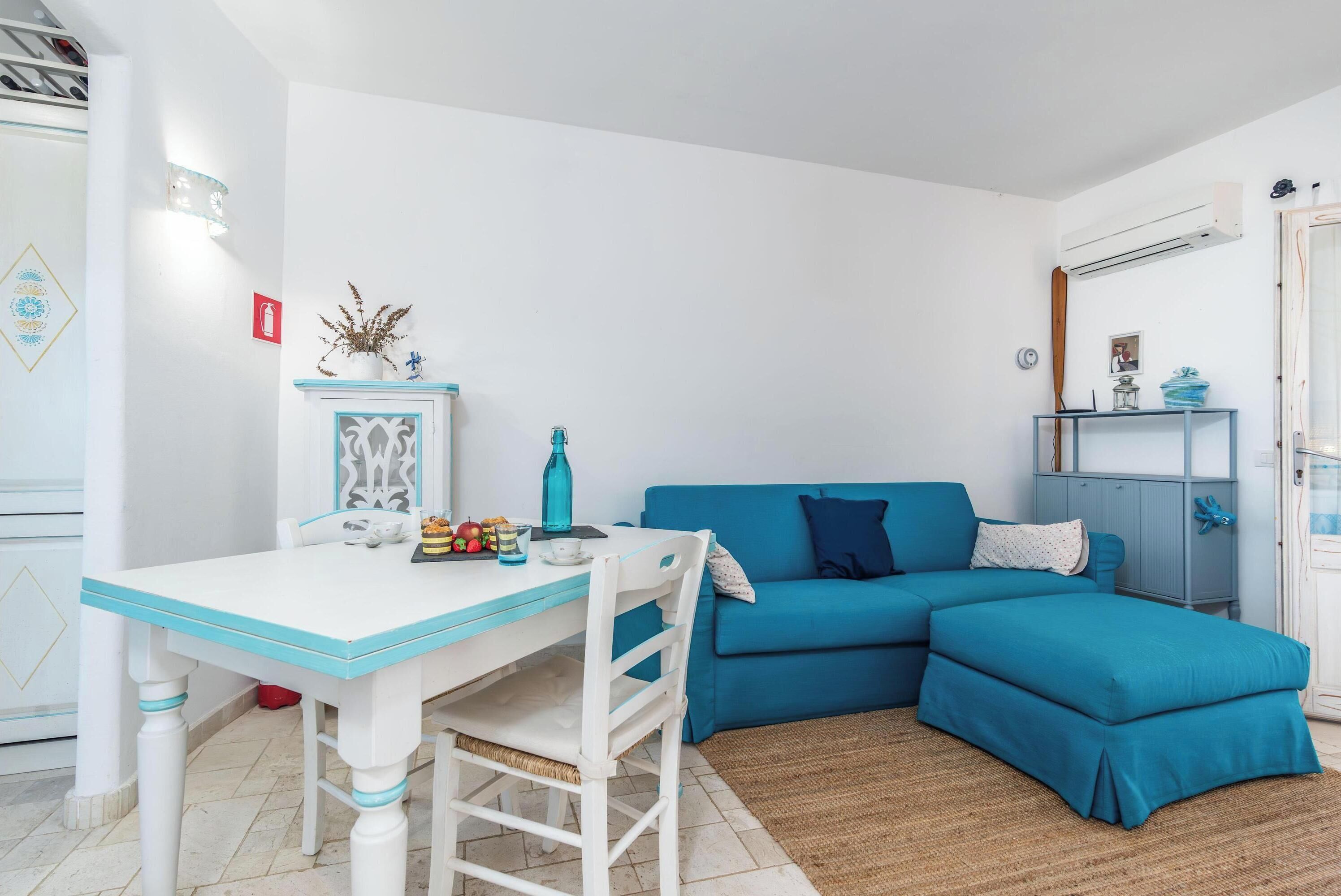 A room with a white table and blue sofa, a small cabinet, and a wall-mounted shelf.