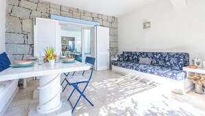 Een lichte, open woonruimte met een stenen muur, een witte bank met bloemenprint in blauw, en een eettafel met blauwe stoelen.
