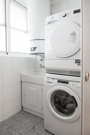 A compact laundry area with a stacked washer and dryer, a small sink, and tiled walls. - GuestReady - Panoramic Ocean View Duplex (Lavra)