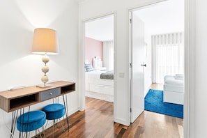 A modern bedroom with a wooden desk, two blue chairs, a lamp, and a bed with white bedding. - GuestReady - Panoramic Ocean View Duplex (Lavra)