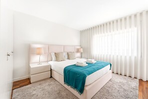A modern bedroom with a large bed, white walls, and a window with sheer curtains. - GuestReady - Panoramic Ocean View Duplex (Lavra)