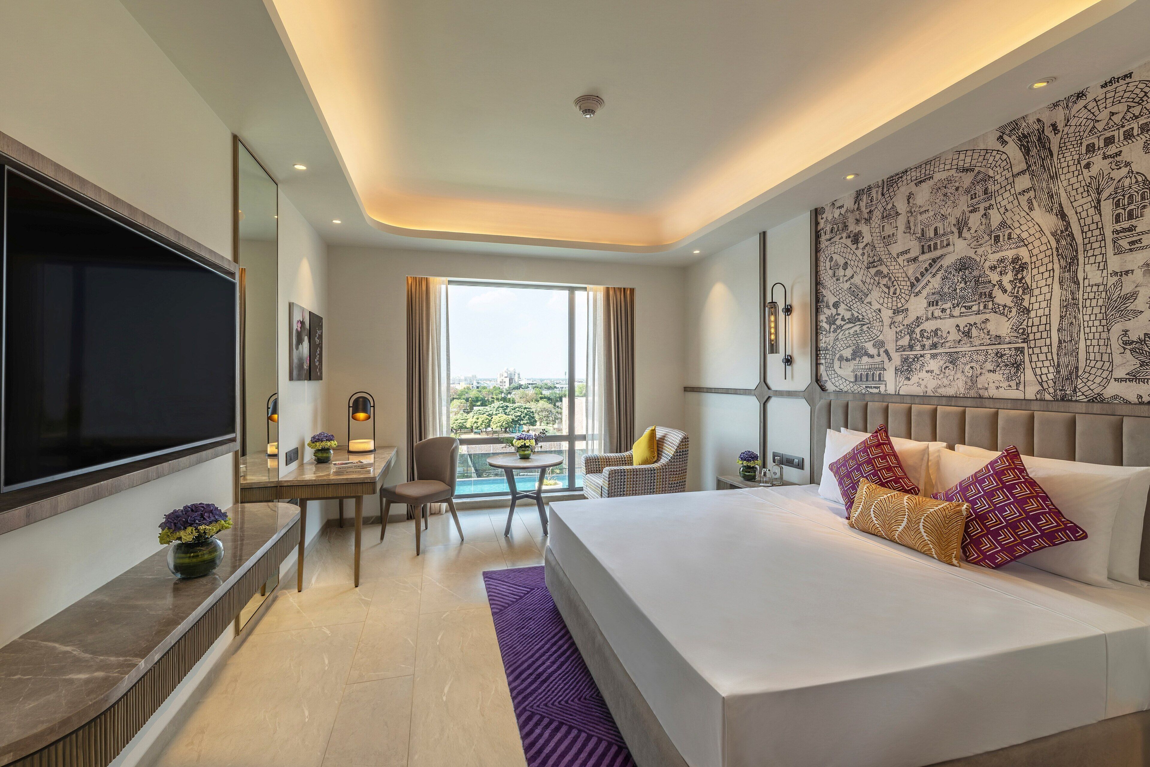 A modern hotel room with a large bed, a desk, a chair, a TV, and a balcony with a view.