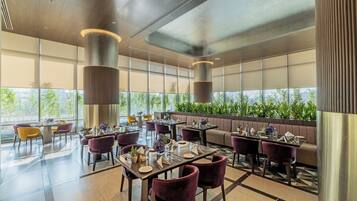 Un comedor moderno con mesas y sillas, ventanas amplias y vistas al verdor exterior.