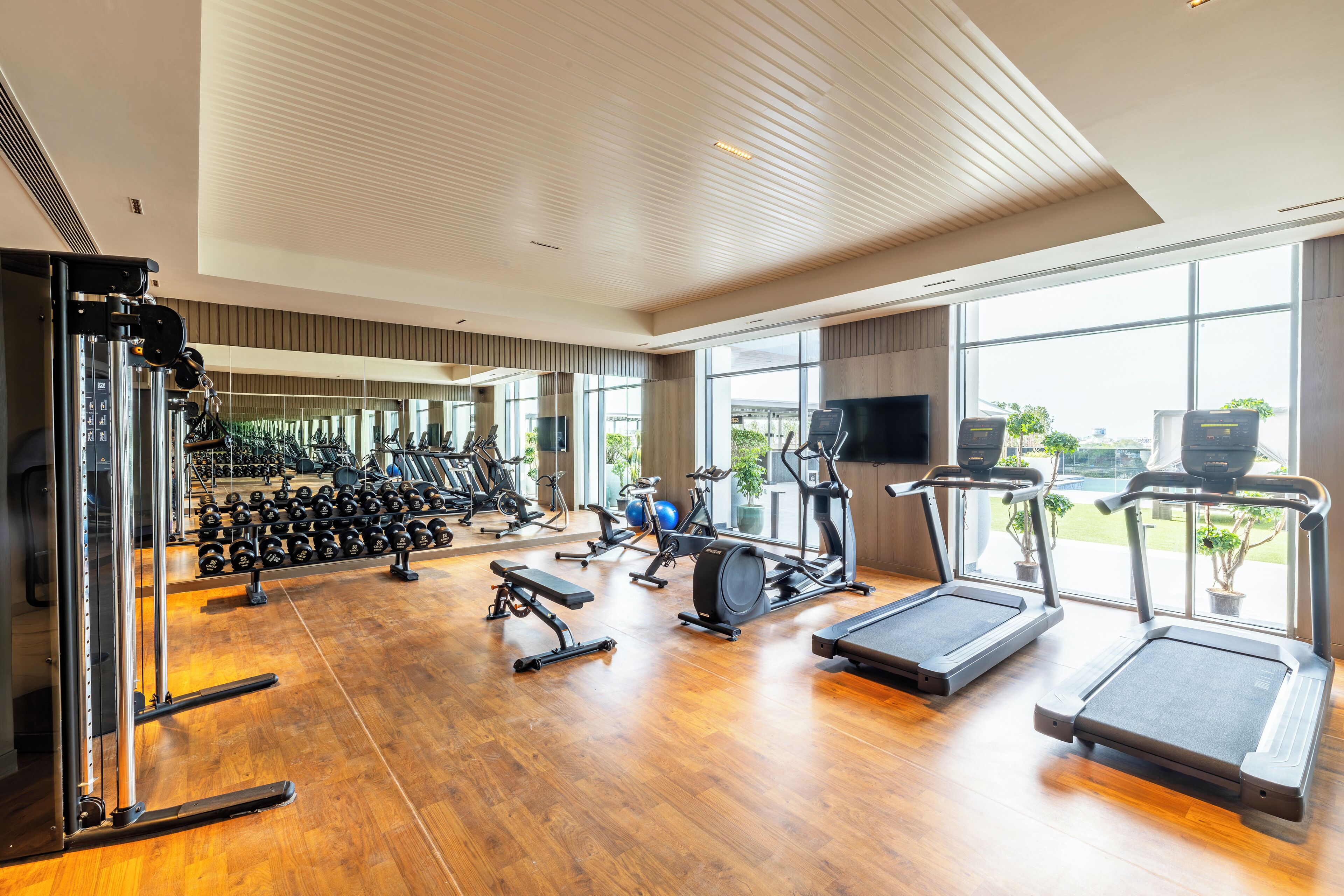 A gym with exercise equipment, large windows, and a wooden floor.