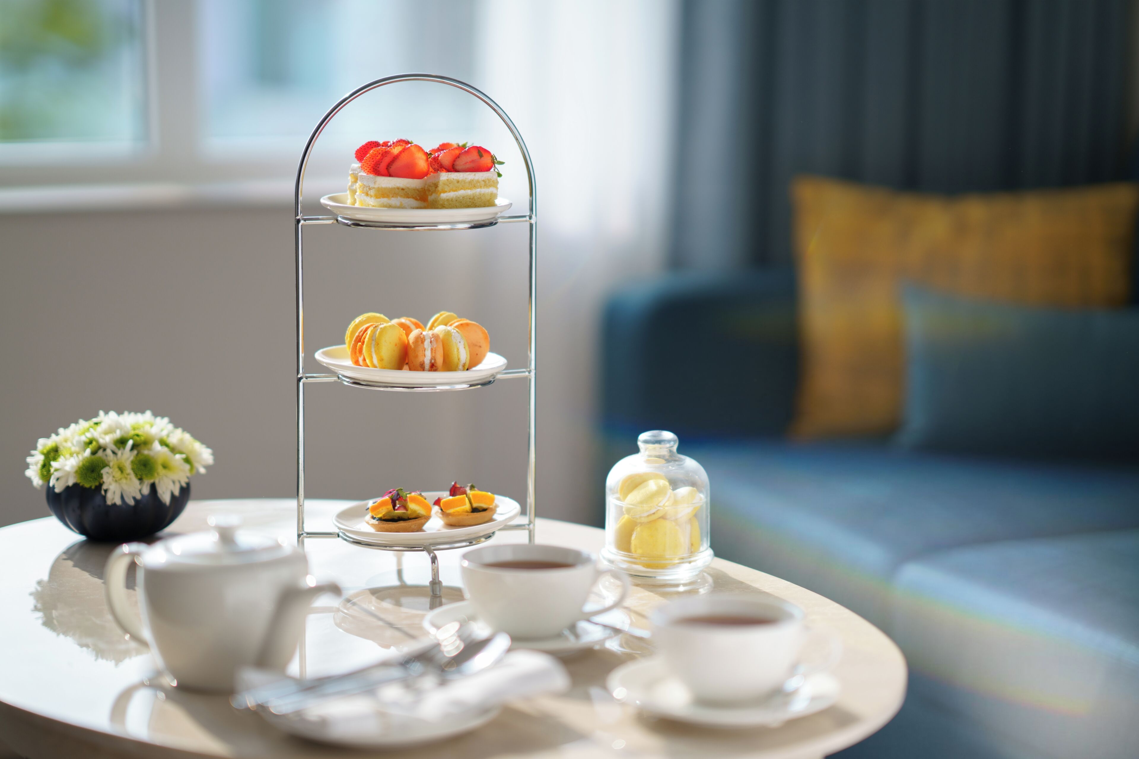 A three-tiered dessert stand with pastries and a glass container of yellow items on a table.