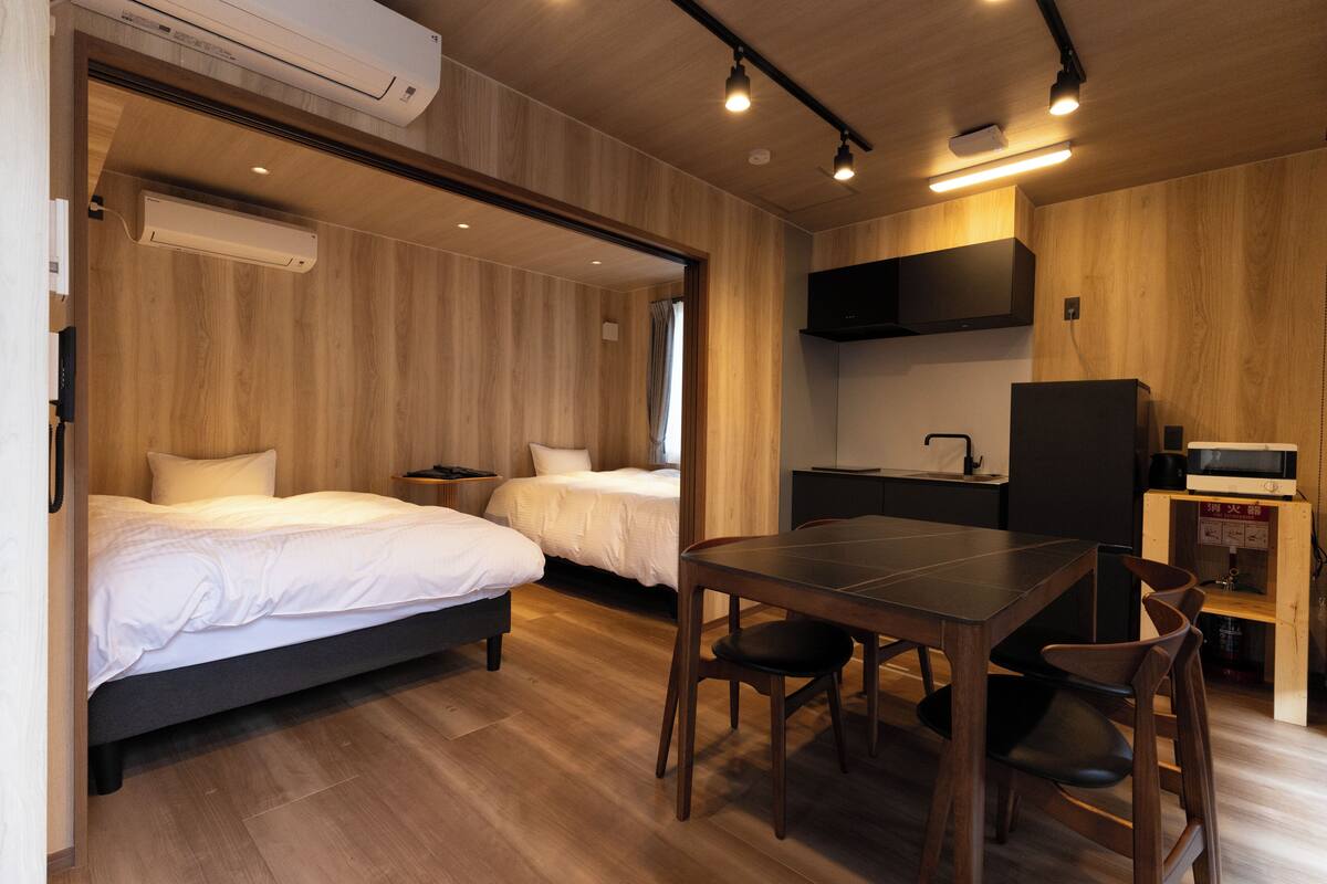 A hotel room with two beds, a dining table, chairs, a TV, and a microwave.