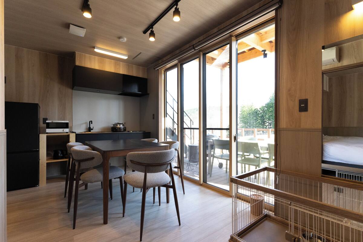 A modern kitchen with a dining area, large windows, and a staircase leading to an upper level.