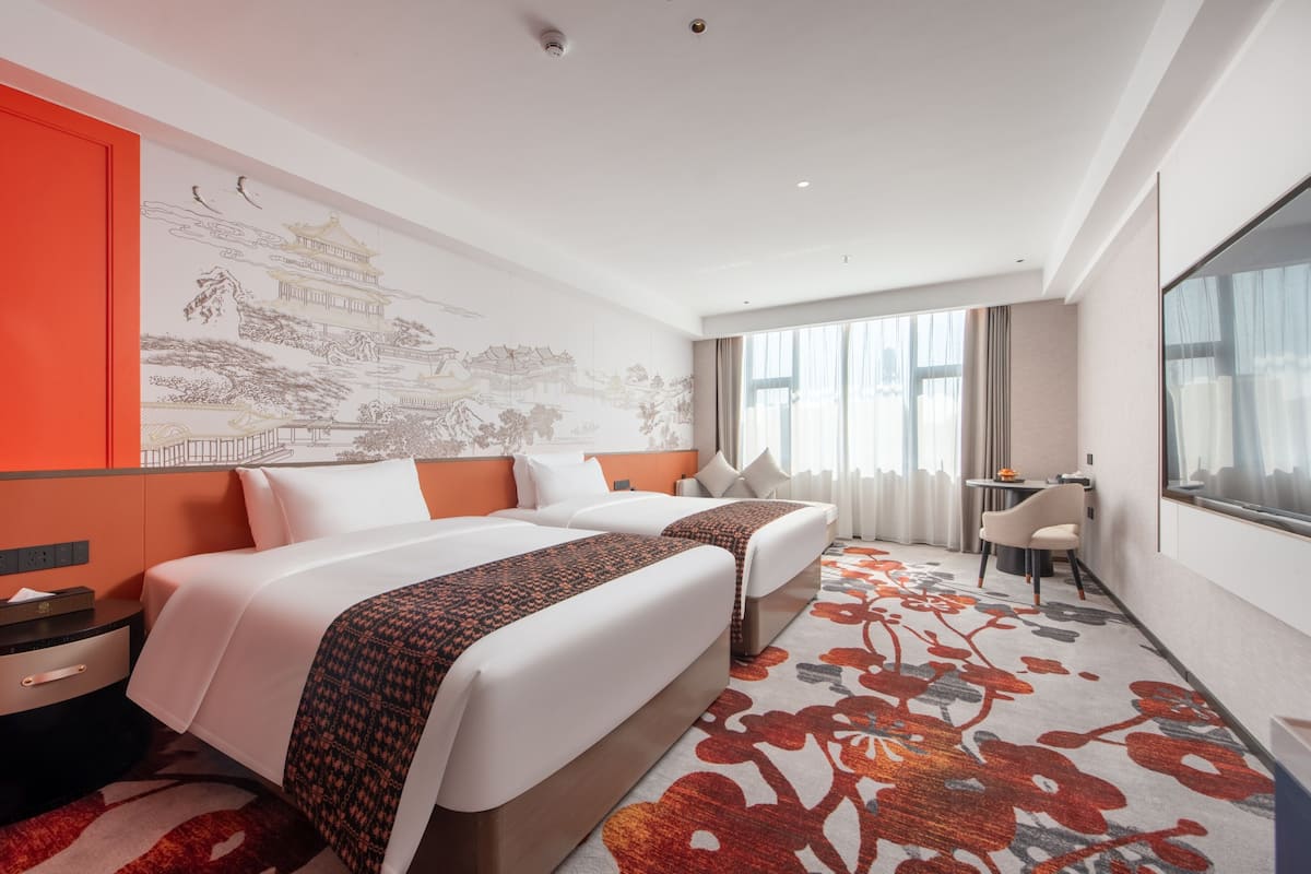 Ein Hotelzimmer mit zwei Betten, einem Schreibtisch und einem großen Fenster.