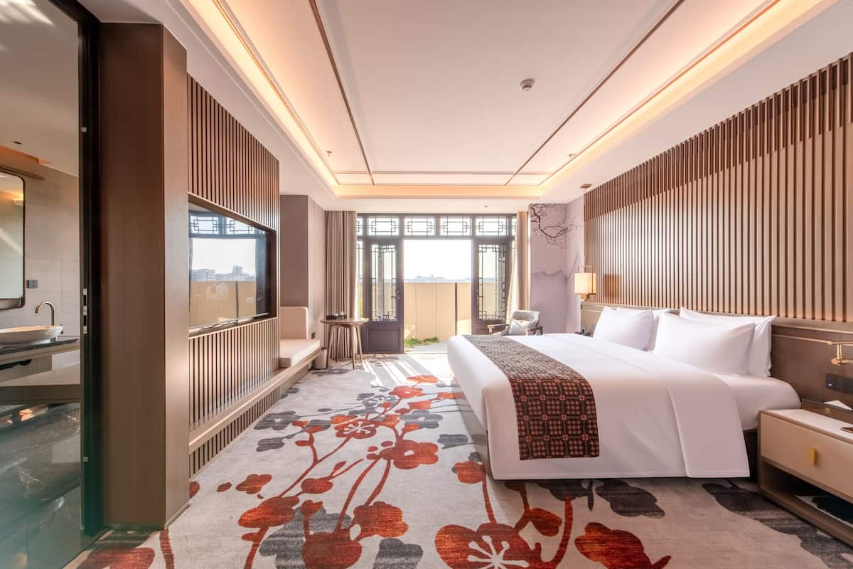 Ein modernes Hotelzimmer mit einem großen Bett, einem Fernseher, einem Badezimmer mit Duschkabine und Blick auf die Stadt.