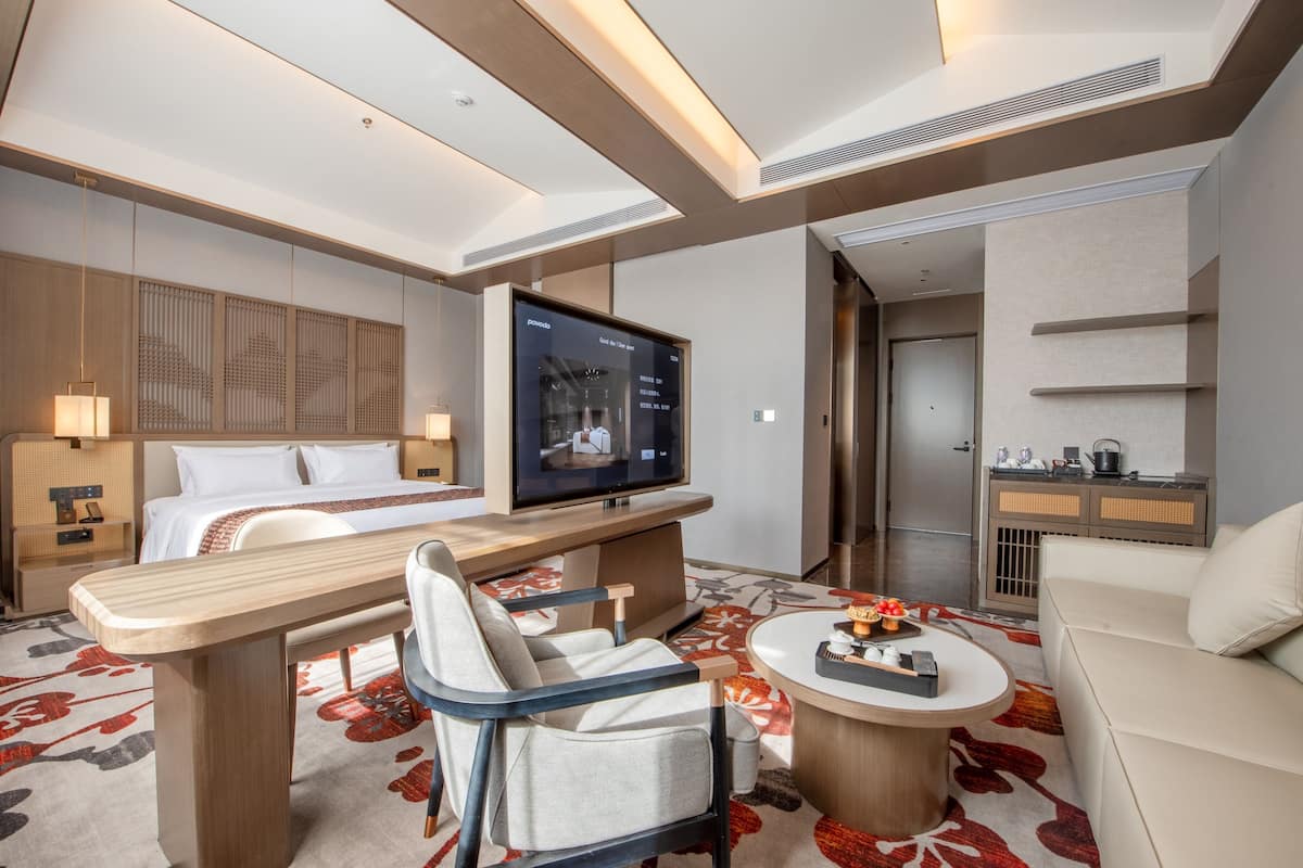 Ein modernes Hotelzimmer mit Bett, Schreibtisch mit Stuhl, Fernseher, Sofa und einer kleinen Küchenzeile.