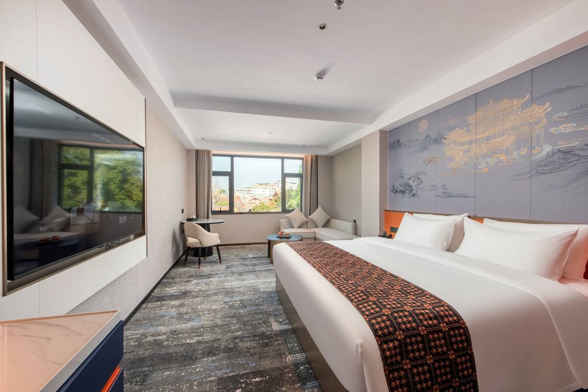 Ein Hotelzimmer mit einem großen Bett, einem Flachbildfernseher, einem Schreibtisch und Blick auf die Stadt durch das Fenster.