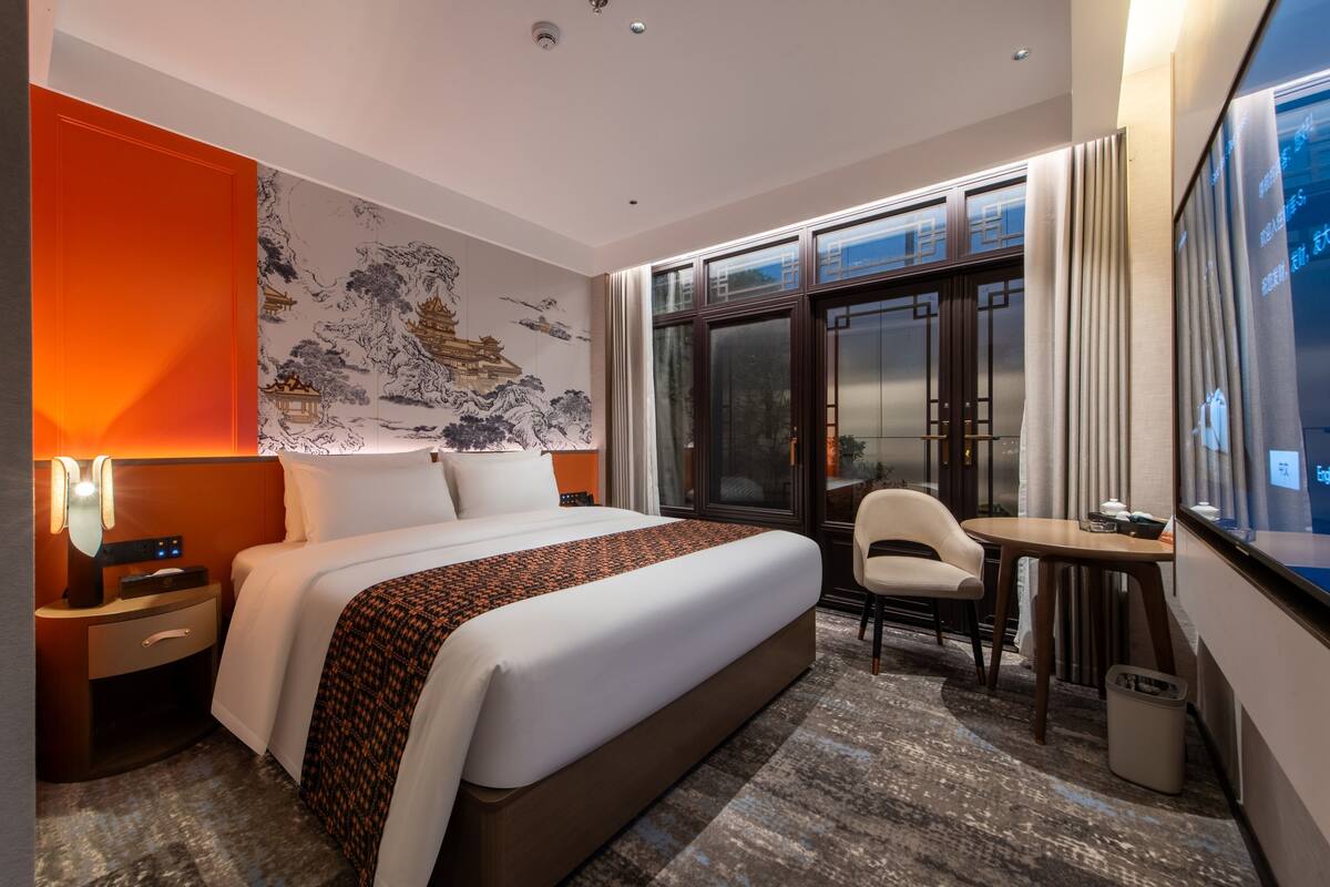 Ein Hotelzimmer mit einem großen Bett, einem Schreibtisch, einem Stuhl und Blick durch eine Glastür nach draußen.
