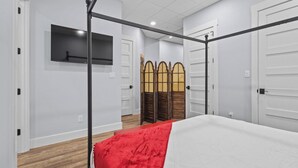 Une chambre à coucher avec un lit à baldaquin, un téléviseur à écran plat fixé au mur et une porte-moustiquaire traditionnelle en bois.