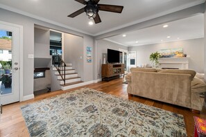 A spacious living area with hardwood flooring, a large beige sofa, a ceiling fan, and a fireplace. - Resort-Style Pool with Slide and Diving Board• 3BR (Long Beach)