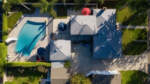 Vue aérienne d’un quartier résidentiel avec une piscine, deux maisons et de la végétation environnante.