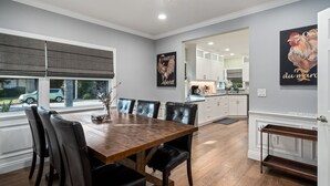 Un coin repas avec une table en bois et des chaises noires, un lustre et une cuisine en arrière-plan.