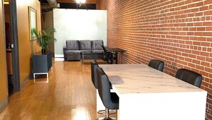 Une salle de réunion moderne avec une longue table, des chaises noires, un canapé gris et un mur en briques.