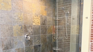 Une douche fermée par des parois de verre, avec un mur carrelé et un tapis bleu sur le sol.