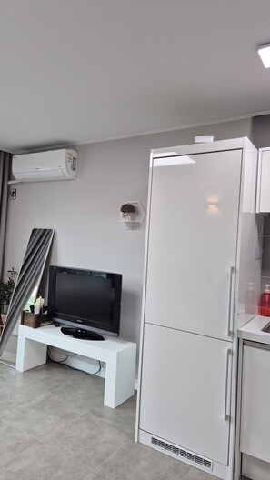 Eine moderne Küche mit einem weißen Kühlschrank, einem Einbauofen und einem Flachbildfernseher auf einem weißen Standfuß.