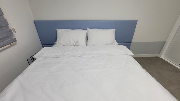 Ein ordentlich bezogenes Bett mit weißen Leinen und einem blauen Kopfteil in einem Hotelzimmer.