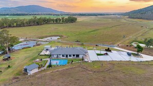 A large, modern building with a swimming pool, surrounded by open fields and a distant mountain range.