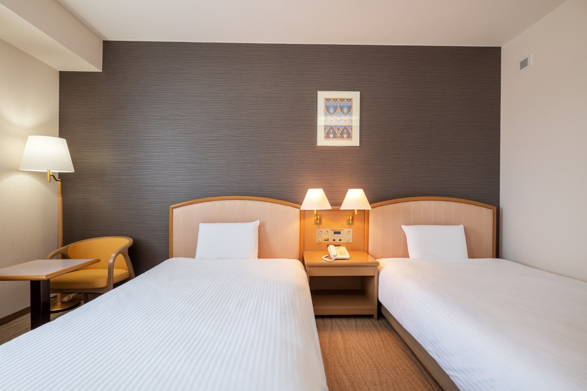 A hotel room with two beds, a desk, a chair, and a wall-mounted telephone.