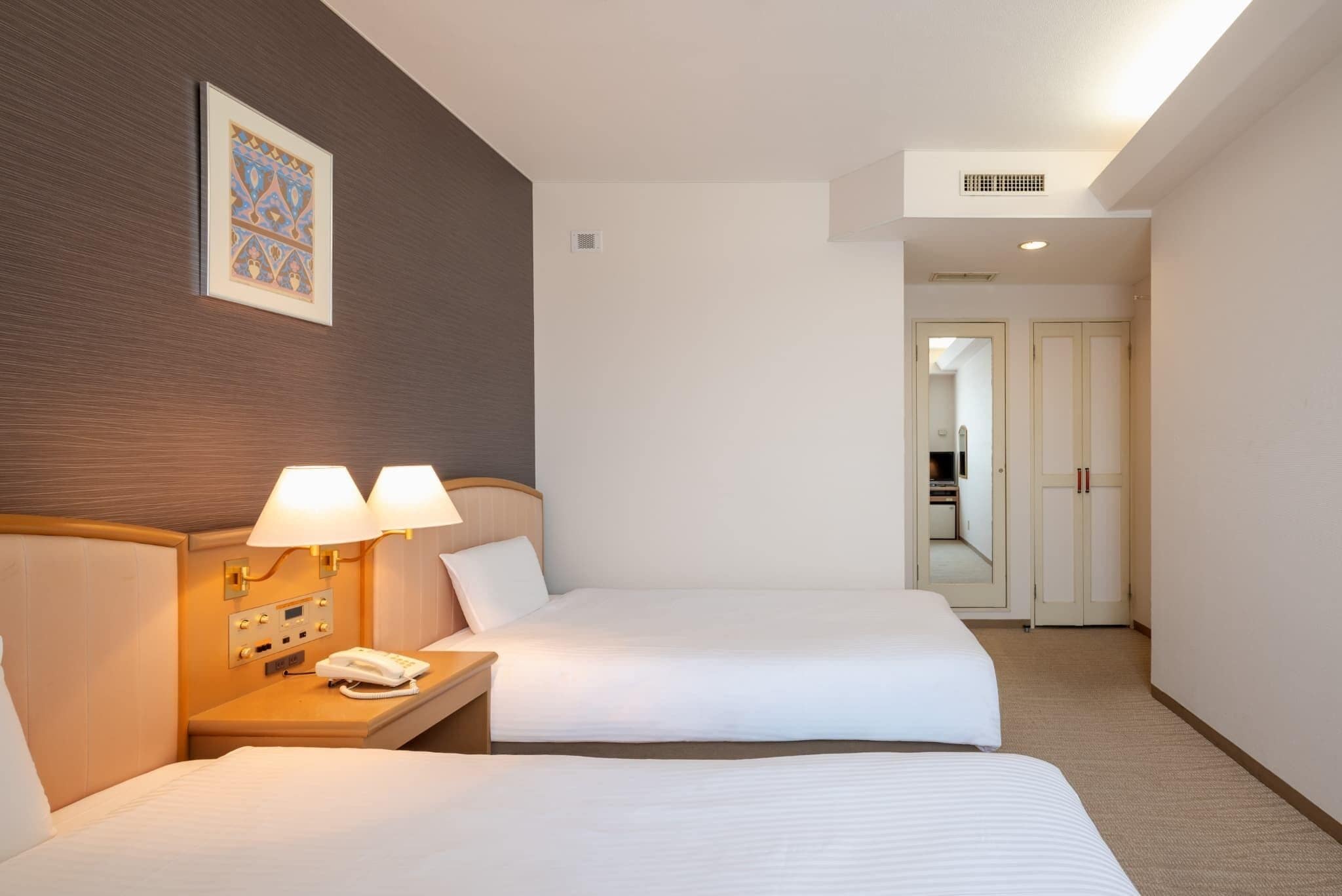 Une chambre d’hôtel avec deux lits, des lampes de chevet, un téléphone et un tableau encadré au mur.