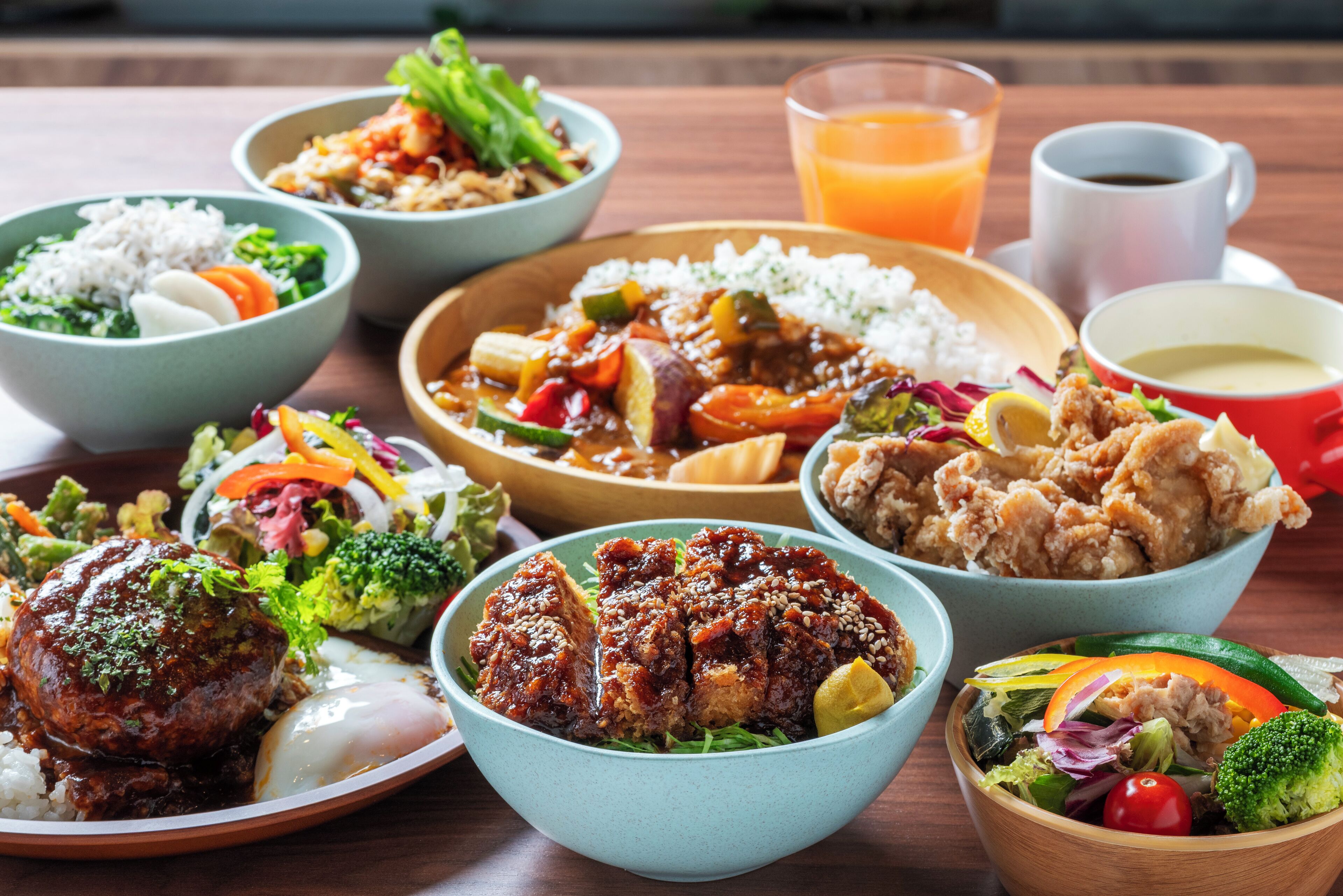 A variety of dishes including rice, vegetables, and meat, served on a wooden table.