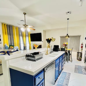 A modern kitchen with a central island, blue cabinets, a ceiling fan, and a flat-screen TV mounted on the wall. - Modern & Cozy Retreat Game Room, Family-Friendly (North Las Vegas)