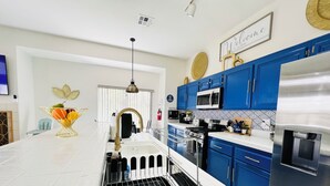 A modern kitchen with a central island, blue cabinets, stainless steel appliances, and a decorative fruit bowl. - Modern & Cozy Retreat Game Room, Family-Friendly (North Las Vegas)