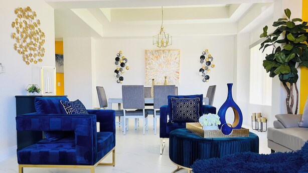 A modern living room with a blue sofa, a grey sofa, and a white sofa. There is a dining table with chairs in the background. - Modern & Cozy Retreat Game Room, Family-Friendly (North Las Vegas)