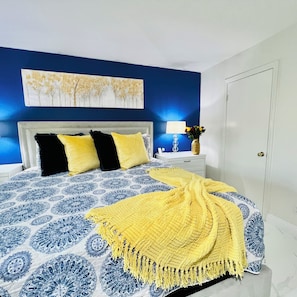 A bedroom with a bed, a nightstand, a lamp, and a door. - Modern & Cozy Retreat Game Room, Family-Friendly (North Las Vegas)