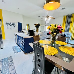 A modern kitchen with a central island, a dining area with yellow placemats, and a ceiling fan. - Modern & Cozy Retreat Game Room, Family-Friendly (North Las Vegas)
